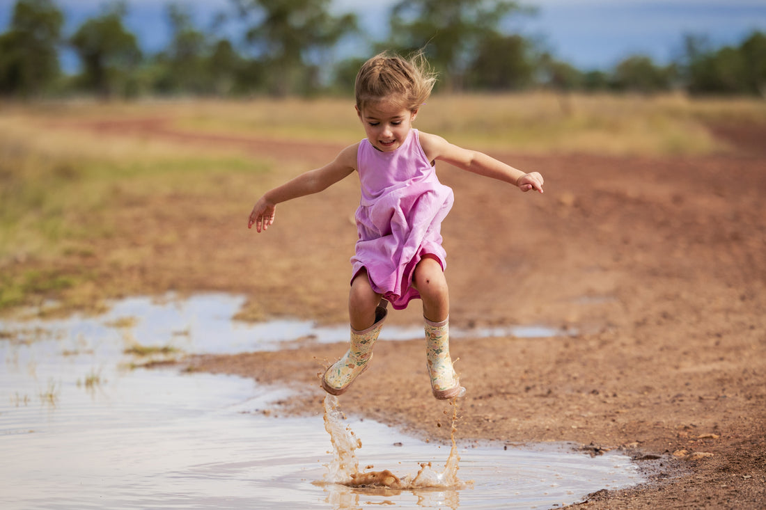 Little girl in pink dress jumping in a puddle