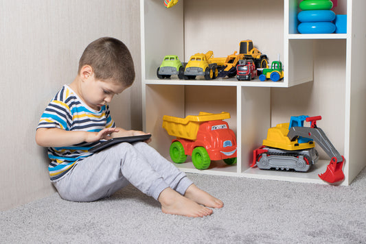 Toddler staring at a screen in front of toys in bedroom
