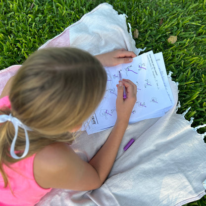 Picture of girl lying on a rug outside with a pink tshirt ticking the worksheet with kangaroos and emus and writing the number on top